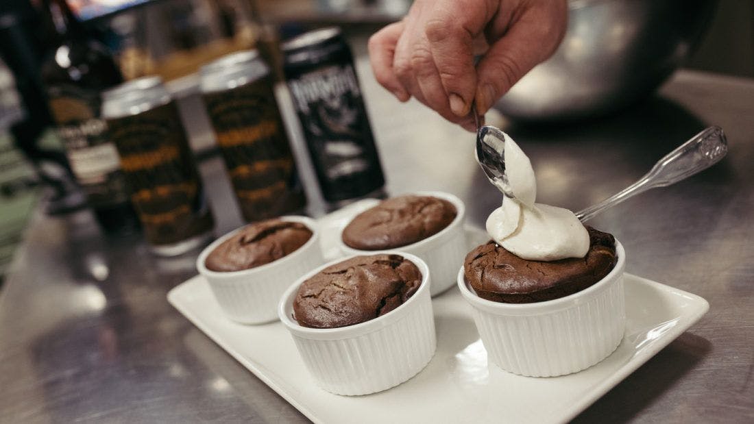 Man placing a dollop of whipped cream onto one of four small cakes