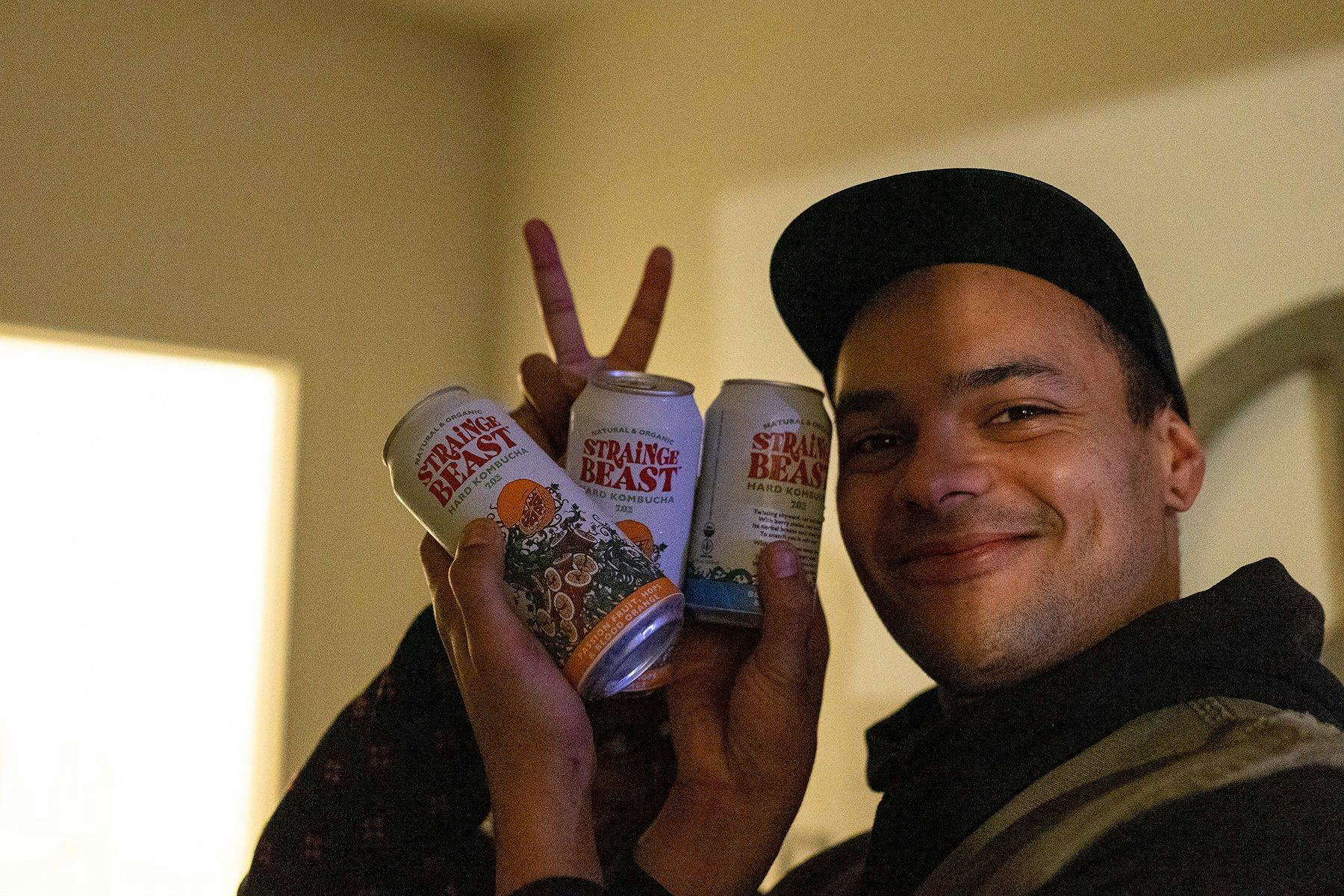 A person holding three cans of Strainge Beast hard kombucha